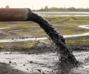 Industrial sludge removal in action with a pipe transferring semi-liquid waste into a containment unit, with workers in protective gear ensuring safe handling.