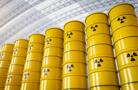 Stacks of yellow hazardous waste barrels with radioactive warning symbols stored in a secure, industrial facility—representing hazardous waste management.